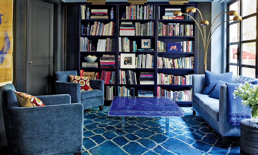 Modern living room with a bold blue vintage rug, velvet seating, built-in bookshelves, and natural light—showcasing how young designers mix vintage elements with contemporary style.